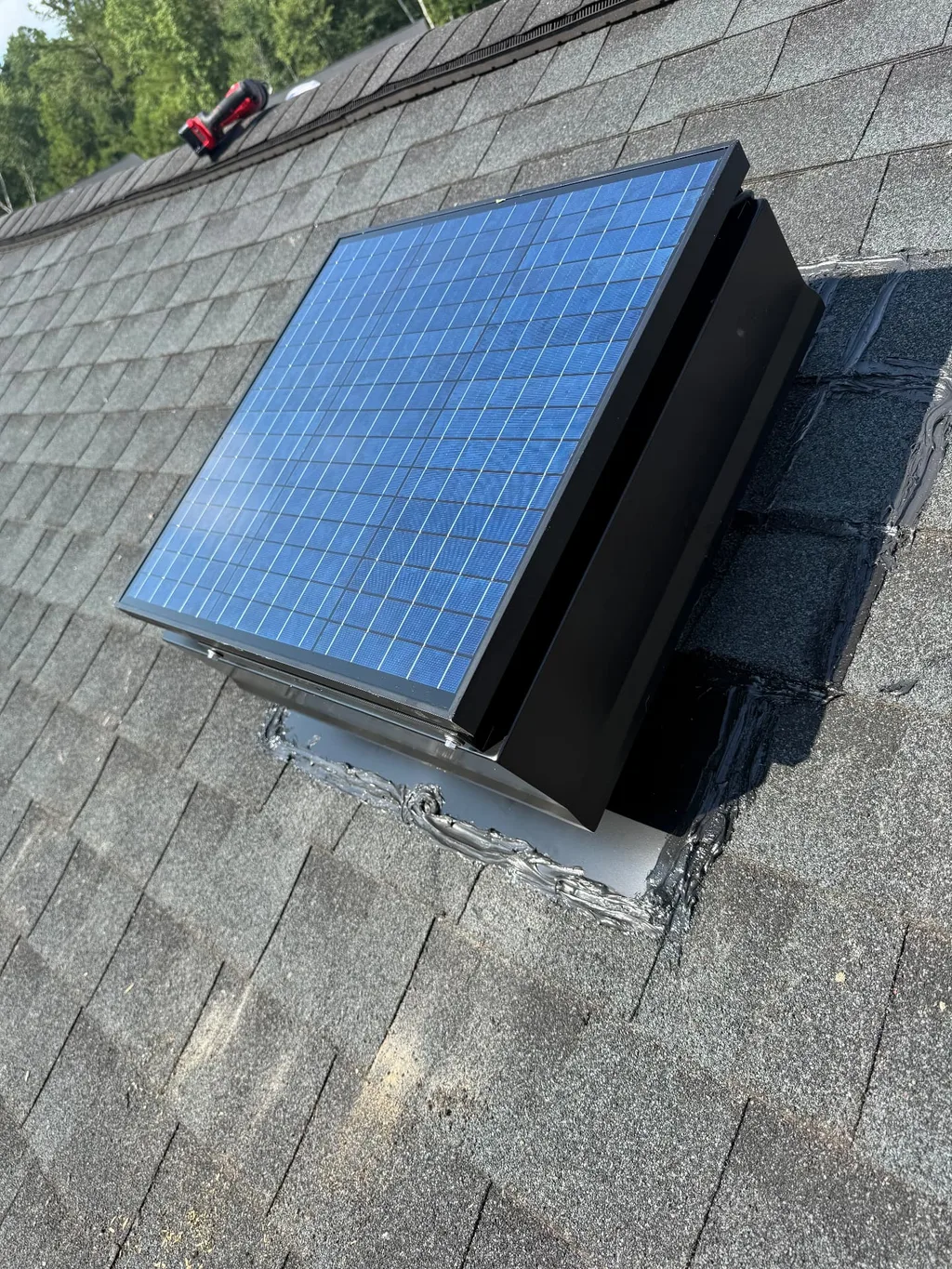 Solar attic fan with a blue photovoltaic panel installed on an asphalt shingle roof