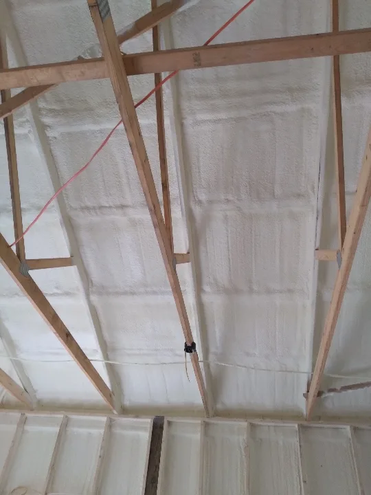 Closed-cell spray foam insulation applied across the underside of an attic roof deck between wooden rafters