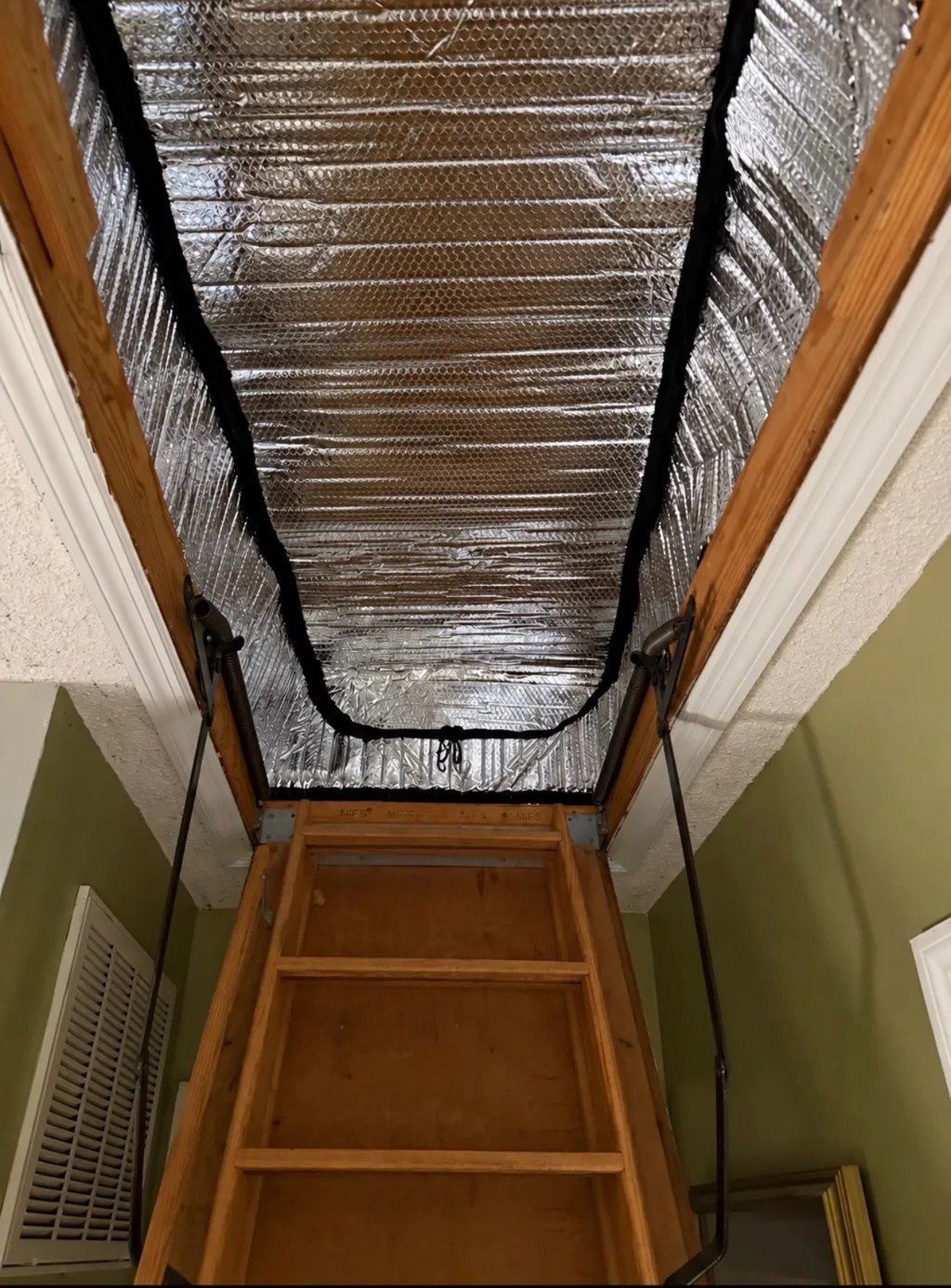 Looking up a pull-down attic ladder into a reflective insulated hatch cover installed over the attic opening