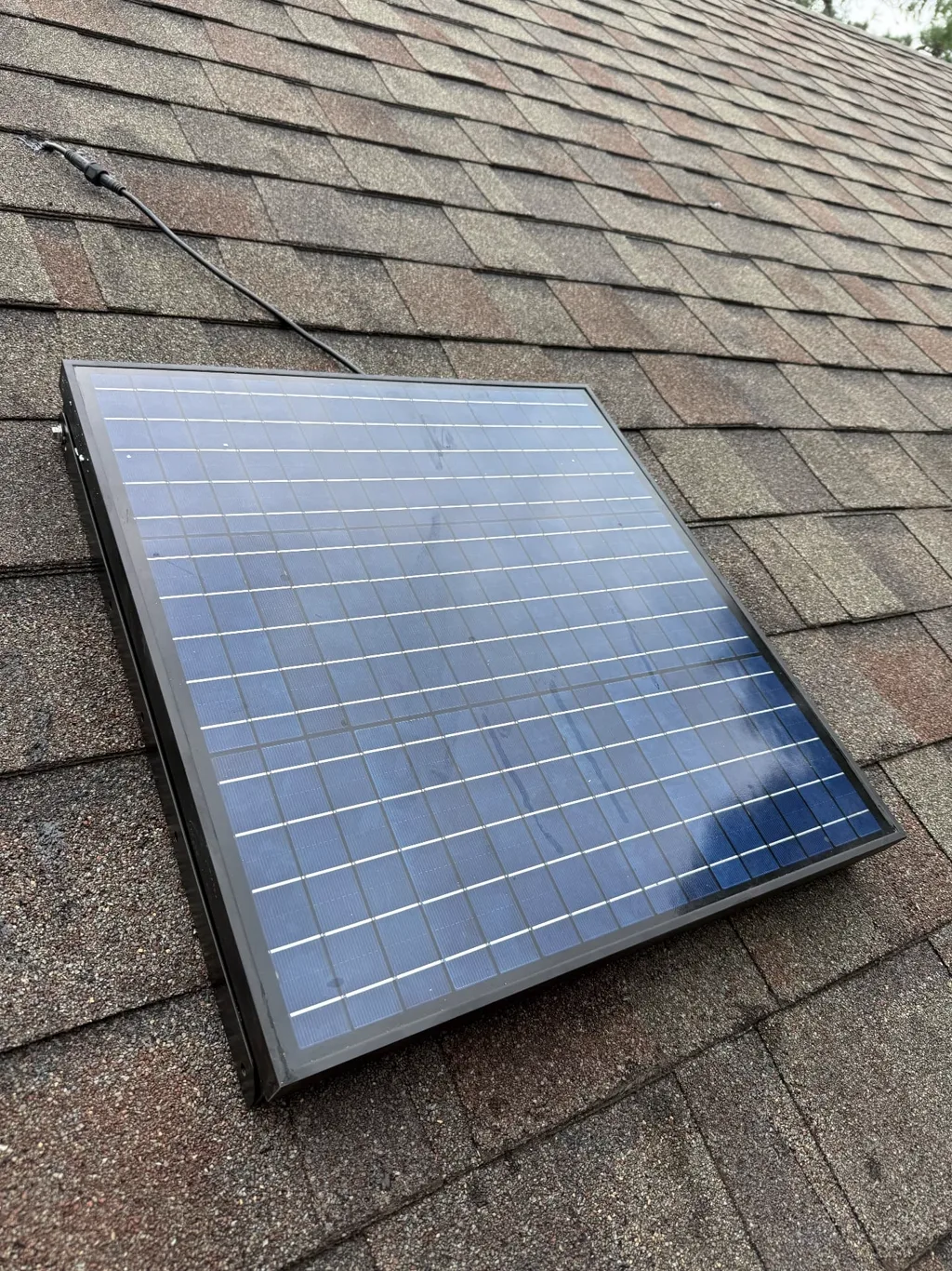 Solar panel positioned on asphalt shingles to power a gable-mounted attic fan