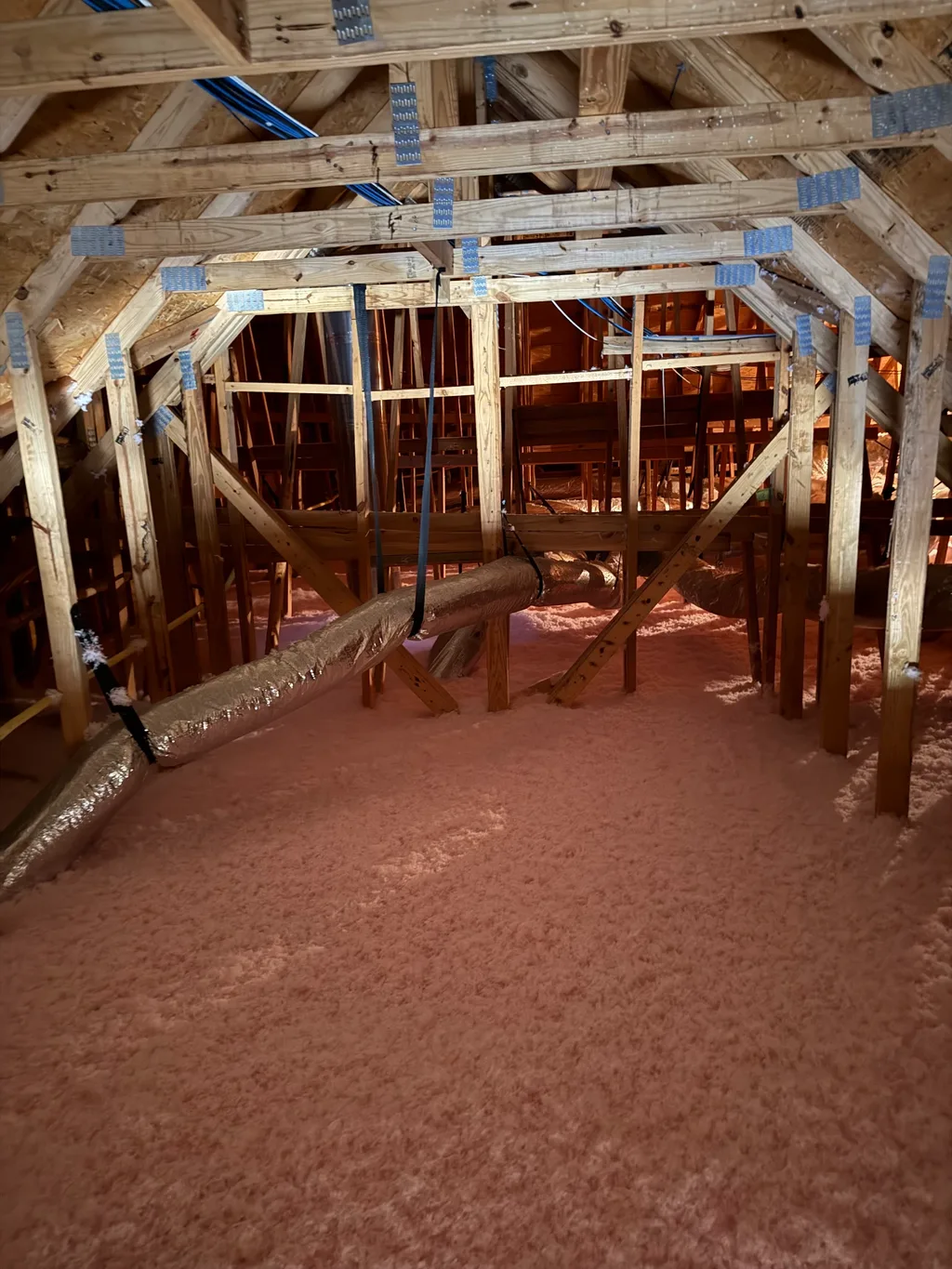 Loose-fill fiberglass insulation blown across an attic floor around framing and flexible ductwork